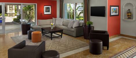 A modern hotel lobby with a beige sofa, dark armchairs, a coffee table, and a patterned rug.