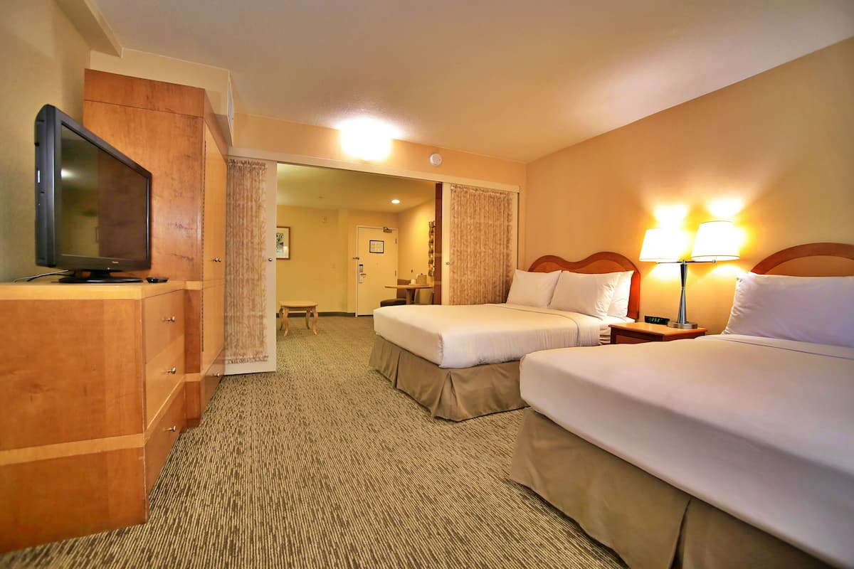 A hotel room with two beds, a TV, a desk, and a lamp.
