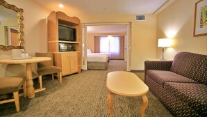 A hotel room with a wooden desk, a television, a sofa, and a bed. - Anaheim Portofino Inn and Suites (Anaheim)