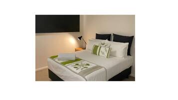 A neatly made bed with white bedding and green accents, a bedside lamp, and a wall-mounted TV.