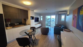 A modern kitchen with a dining area, a TV mounted on the wall, and a balcony with a view.