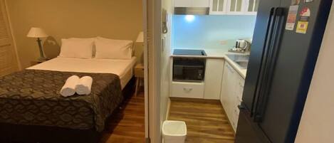 A compact hotel room with a bed, a small kitchenette, and a refrigerator.
