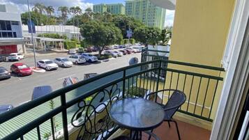 Varanda com mesa e cadeiras, vista para uma rua com carros e edifícios.