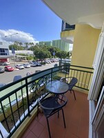 Varanda com mesa e cadeiras, vista para uma rua com carros e edifícios.