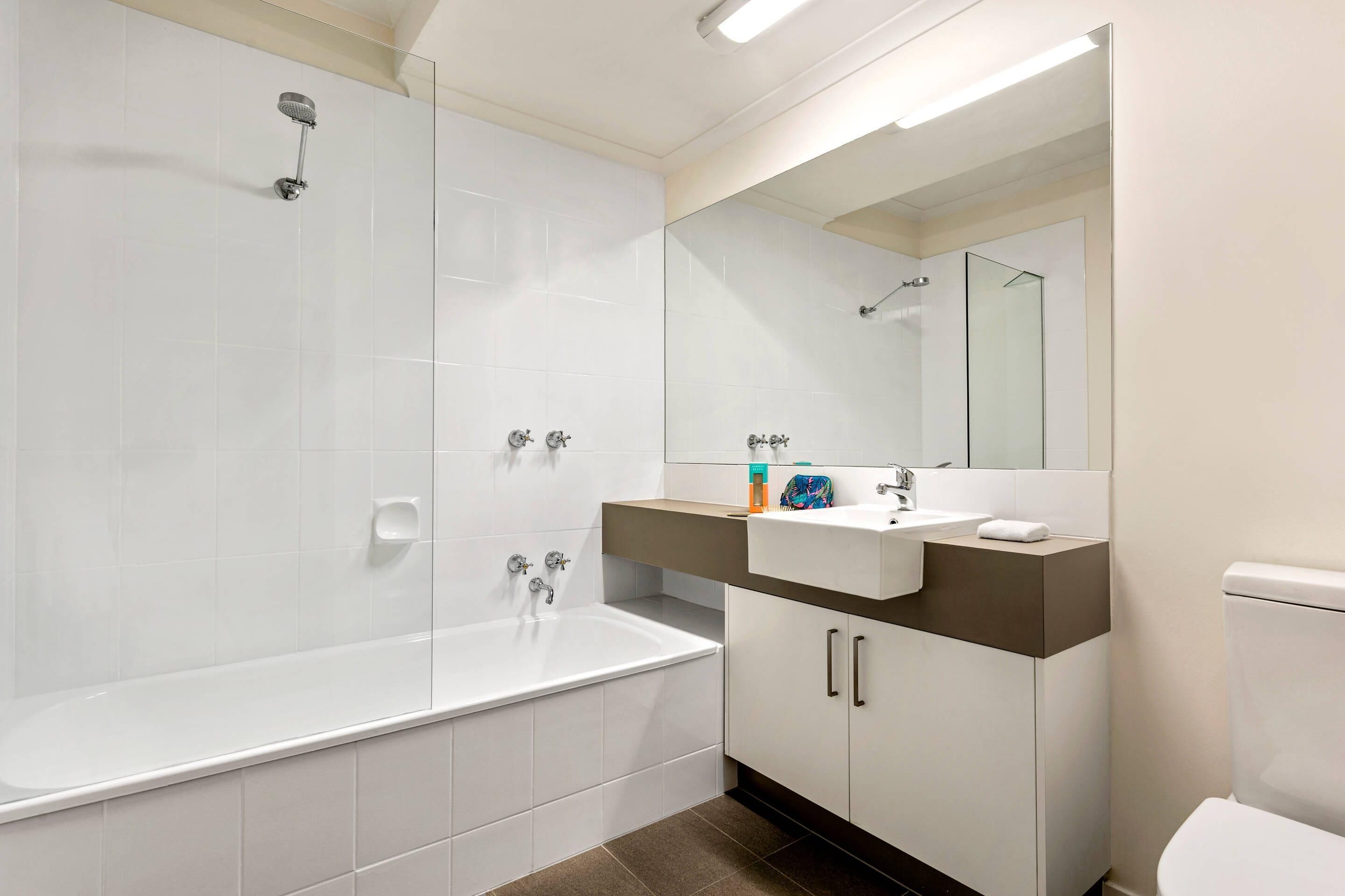A modern bathroom with a bathtub, a glass-enclosed shower, a vanity with a mirror, and a toilet.
