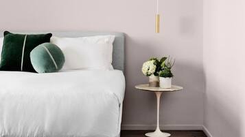 A neatly arranged bedroom with a bed, pillows, a bedside table with a plant, and a hanging light fixture.