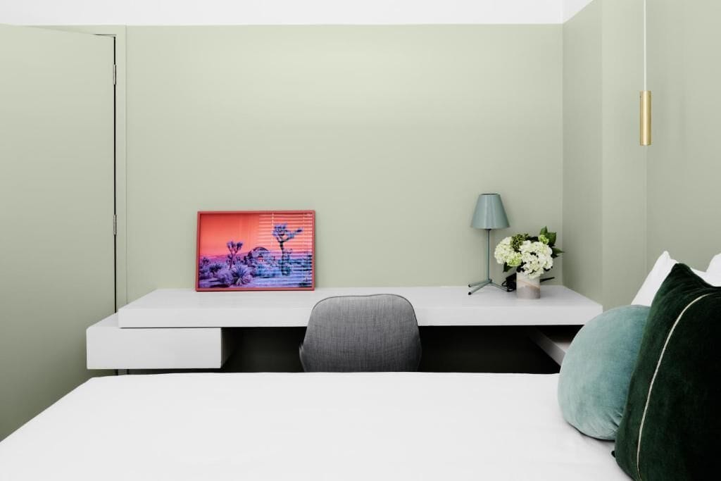 A modern bedroom with a bed, a desk, a chair, a lamp, and a framed picture on the wall.