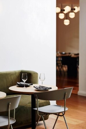 A dining area with a round table, a green upholstered chair, and a modern chandelier.