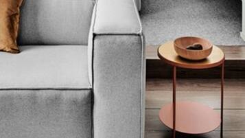 Une chambre moderne avec un lit, un canapé gris et une petite table d’appoint en bois.