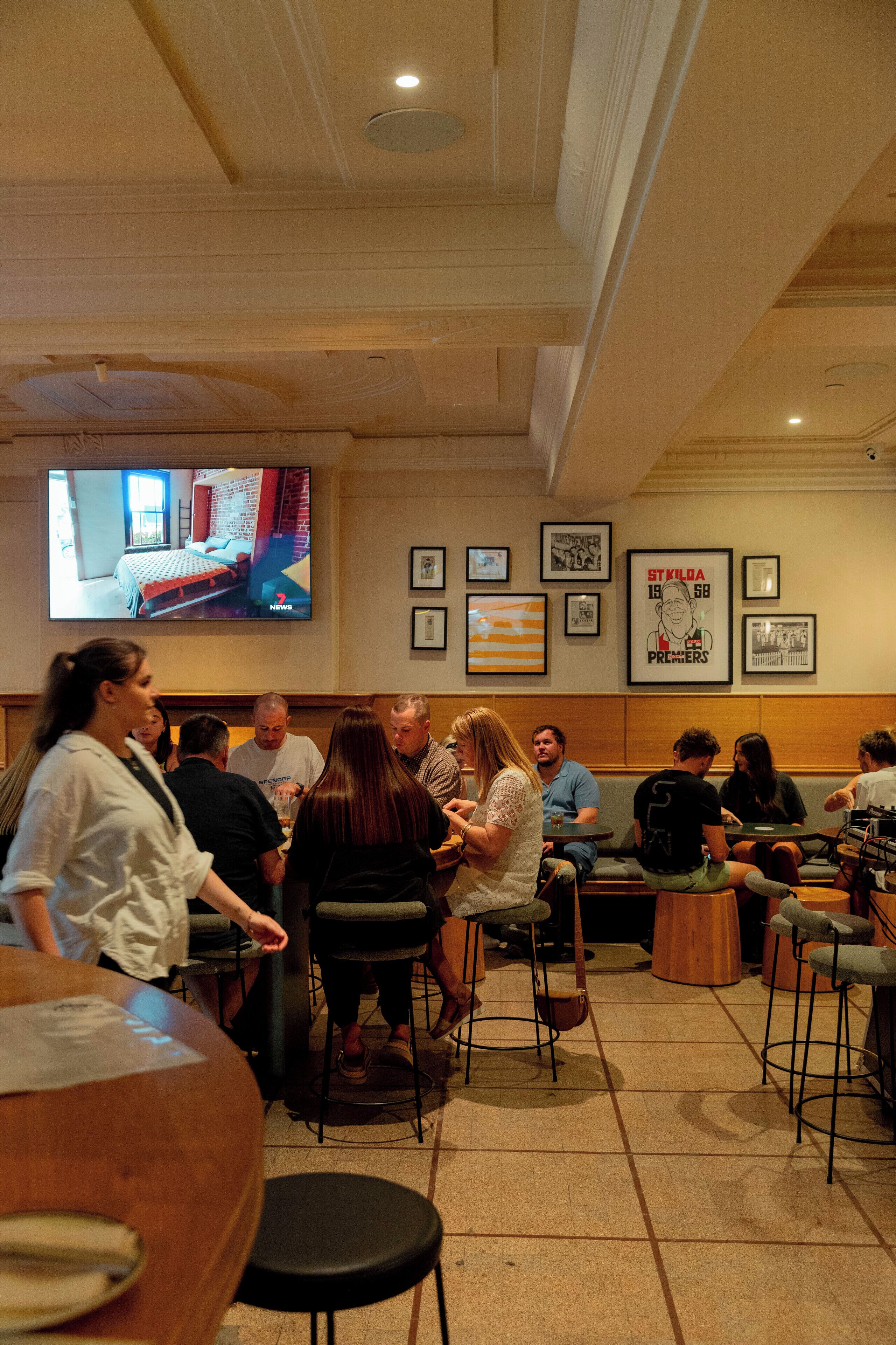 Un restaurante con una pantalla de televisión mostrando una habitación, fotografías enmarcadas en la pared y personas comiendo.