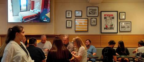 Un restaurante con una pantalla de televisión mostrando una habitación, fotografías enmarcadas en la pared y personas comiendo.