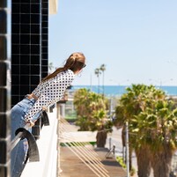 A person leaning on a railing overlooking a coastal area with palm trees and a clear sky.