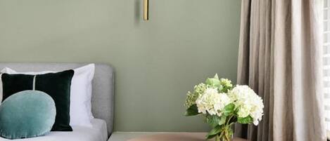 A hotel room with a bed, a round table with a vase of flowers, a chair, and a window with curtains.