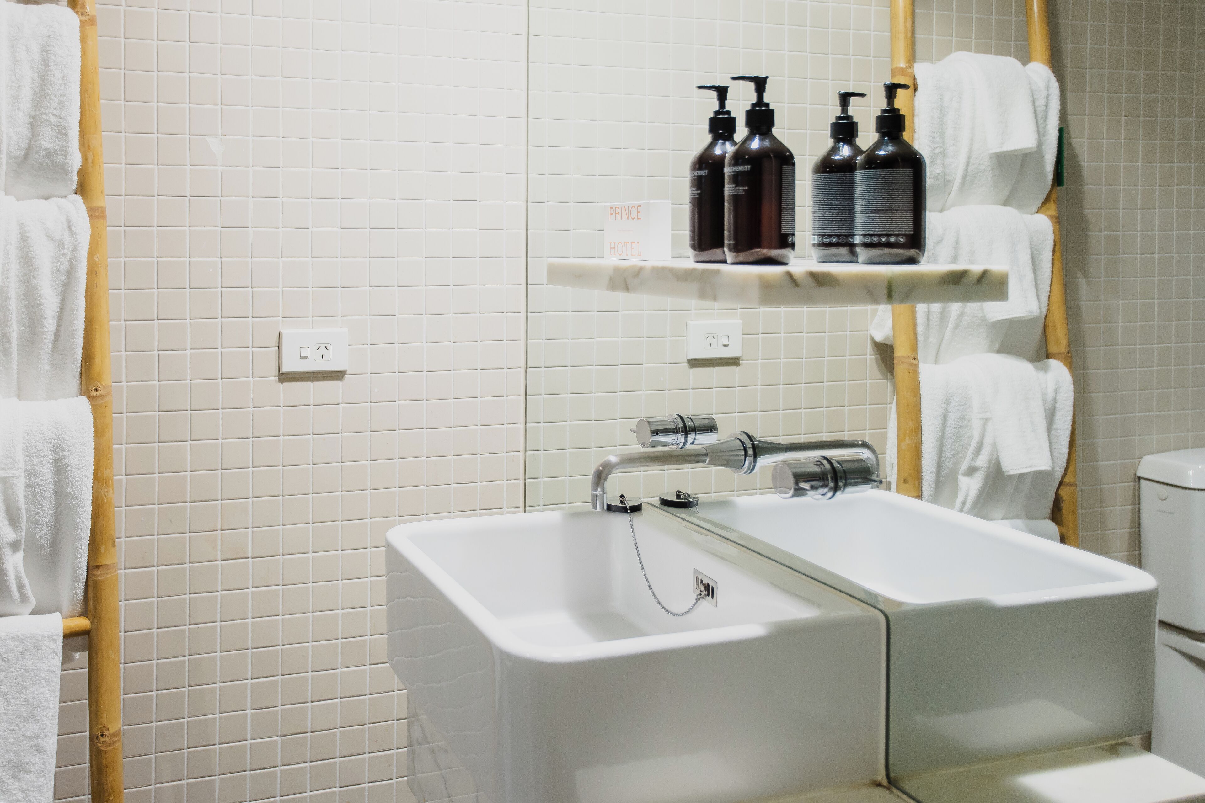 Un baño con lavamanos blanco, un espejo y un estante con artículos de aseo.