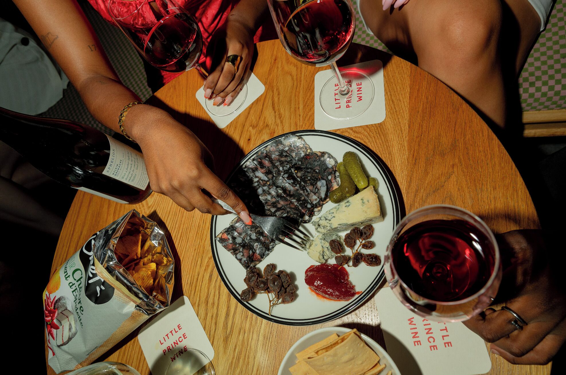 Een ronde houten tafel met een bord eten, een fles wijn en glazen rode wijn.
