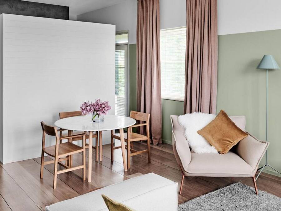 Una sala de estar moderna con una mesa redonda, sillas de madera, un sofá con un cojín marrón, una lámpara de pie y un tapete gris.