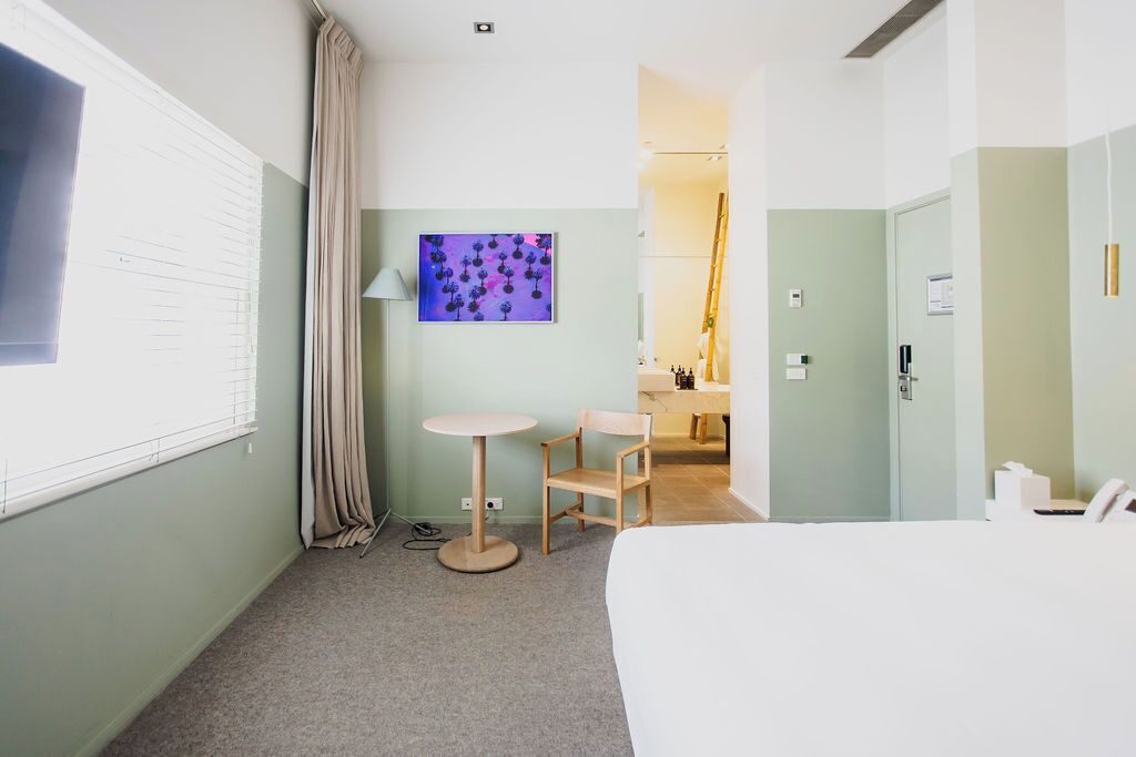 Une chambre d’hôtel avec un lit, une table ronde, une chaise, un bureau, une salle de bain et un tableau au mur.