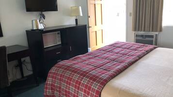 A hotel room with a bed, a desk with a TV, a microwave, and a door leading outside.