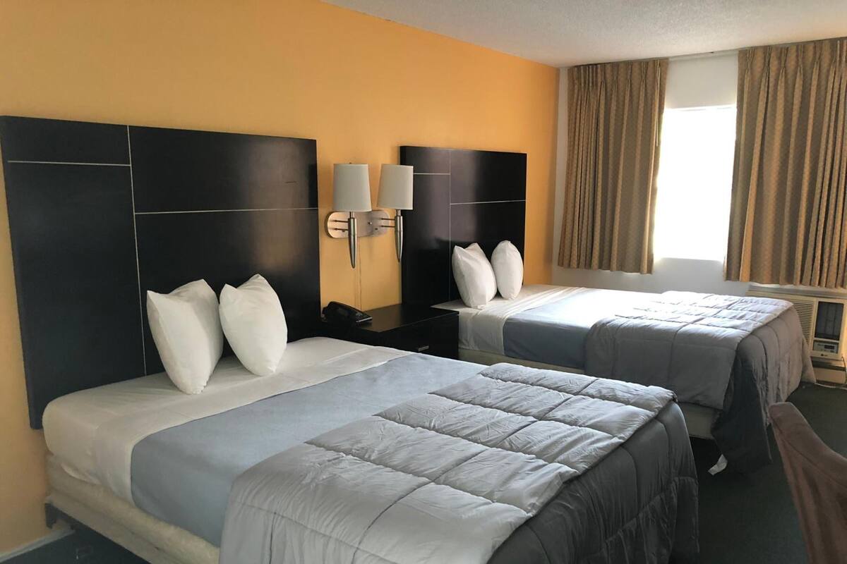 Habitación de hotel con dos camas, un ventanal con cortinas y una lámpara fijada a la pared.