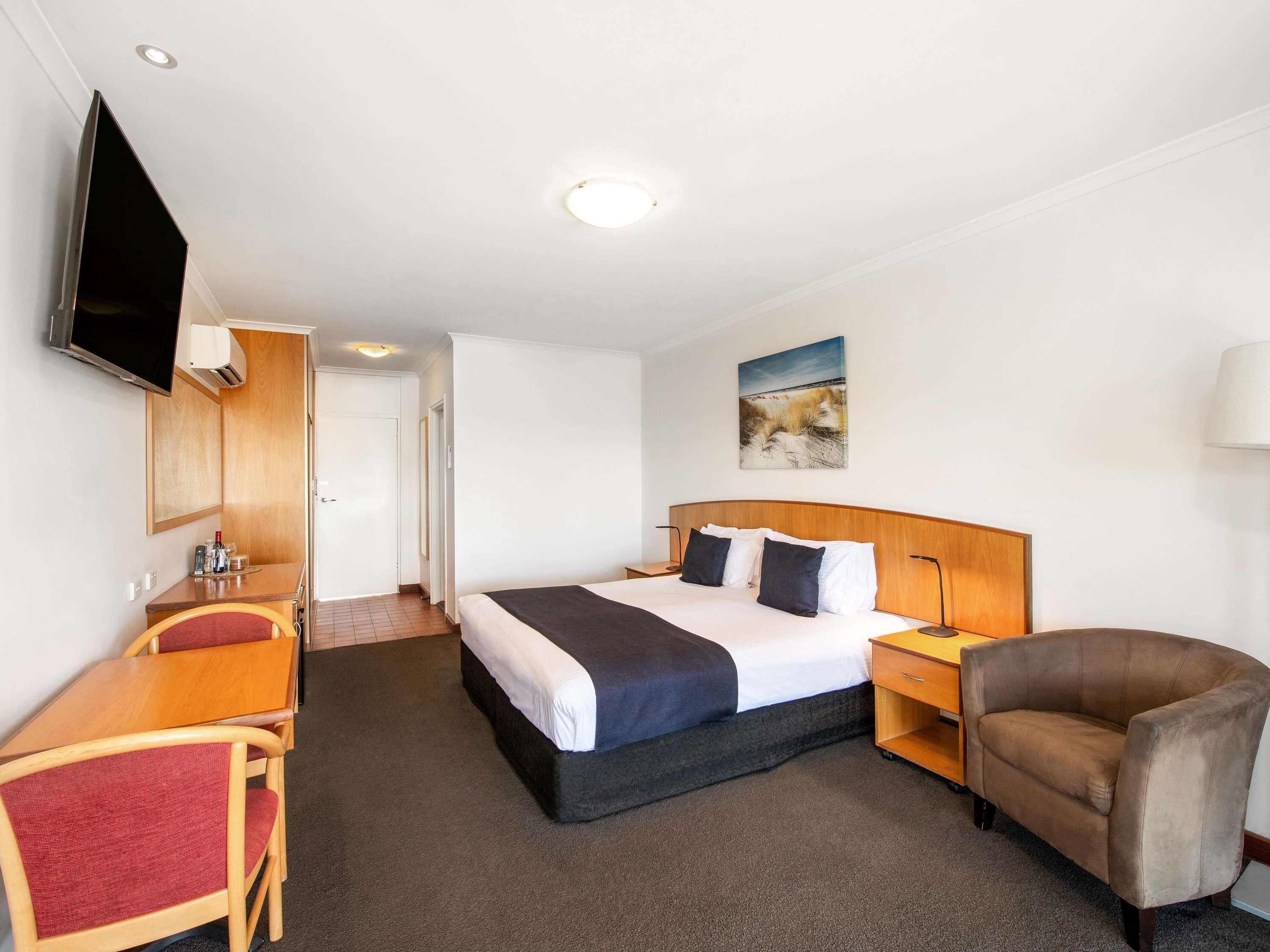 Habitación de hotel con cama, escritorio, silla, televisor y un cuadro en la pared.