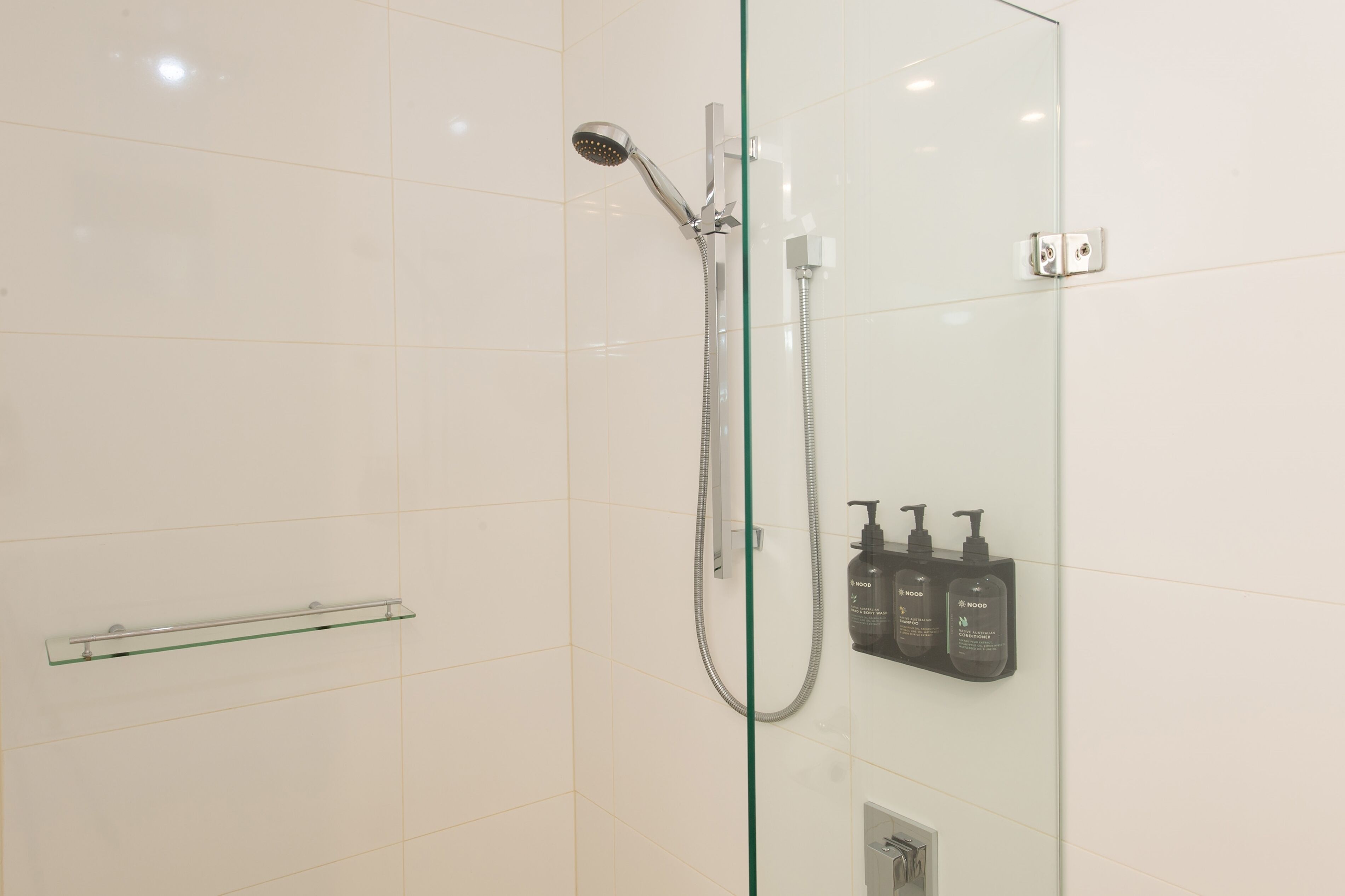 Une douche fermée par des parois en verre, dotée d’un pommeau de douche à main et d’un panneau de commande fixé au mur.
