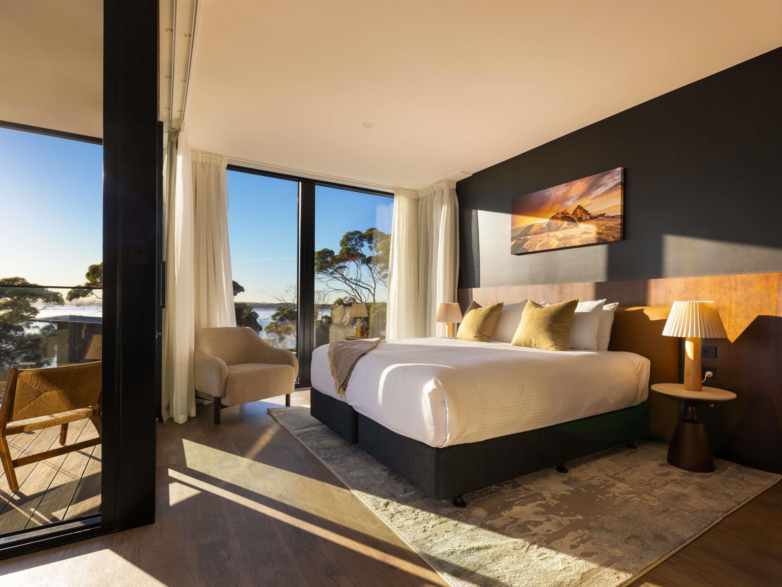 A modern bedroom with a large bed, a chair, and a view of the outdoors.