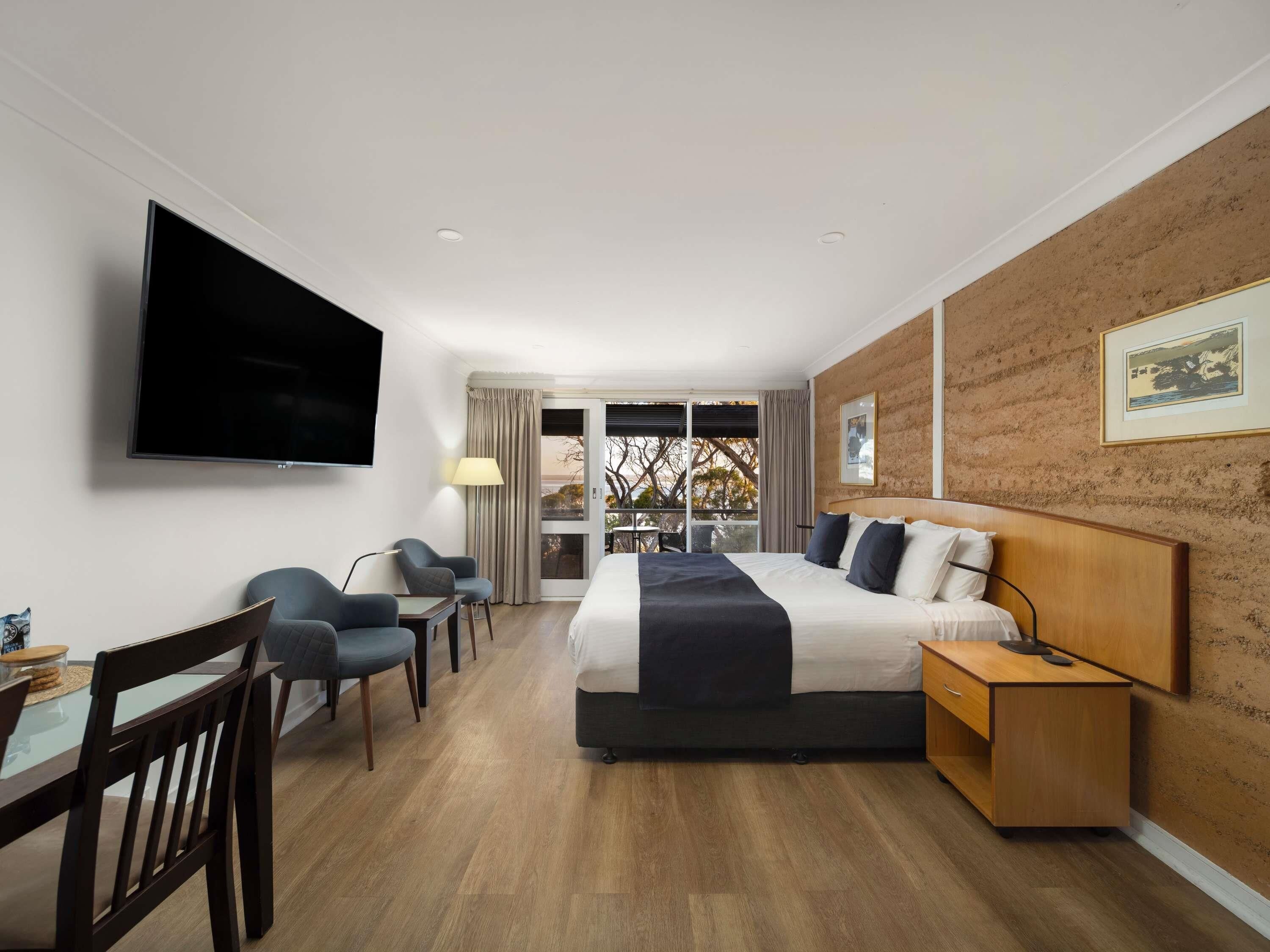 A hotel room with a bed, a desk, a chair, a TV, and a view through a glass door.