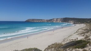 Una playa con aguas turquesas cristalinas, una orilla arenosa y acantilados rocosos al fondo.