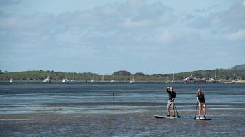 Two people paddleboarding on a calm body of water with boats and a ship in the background.