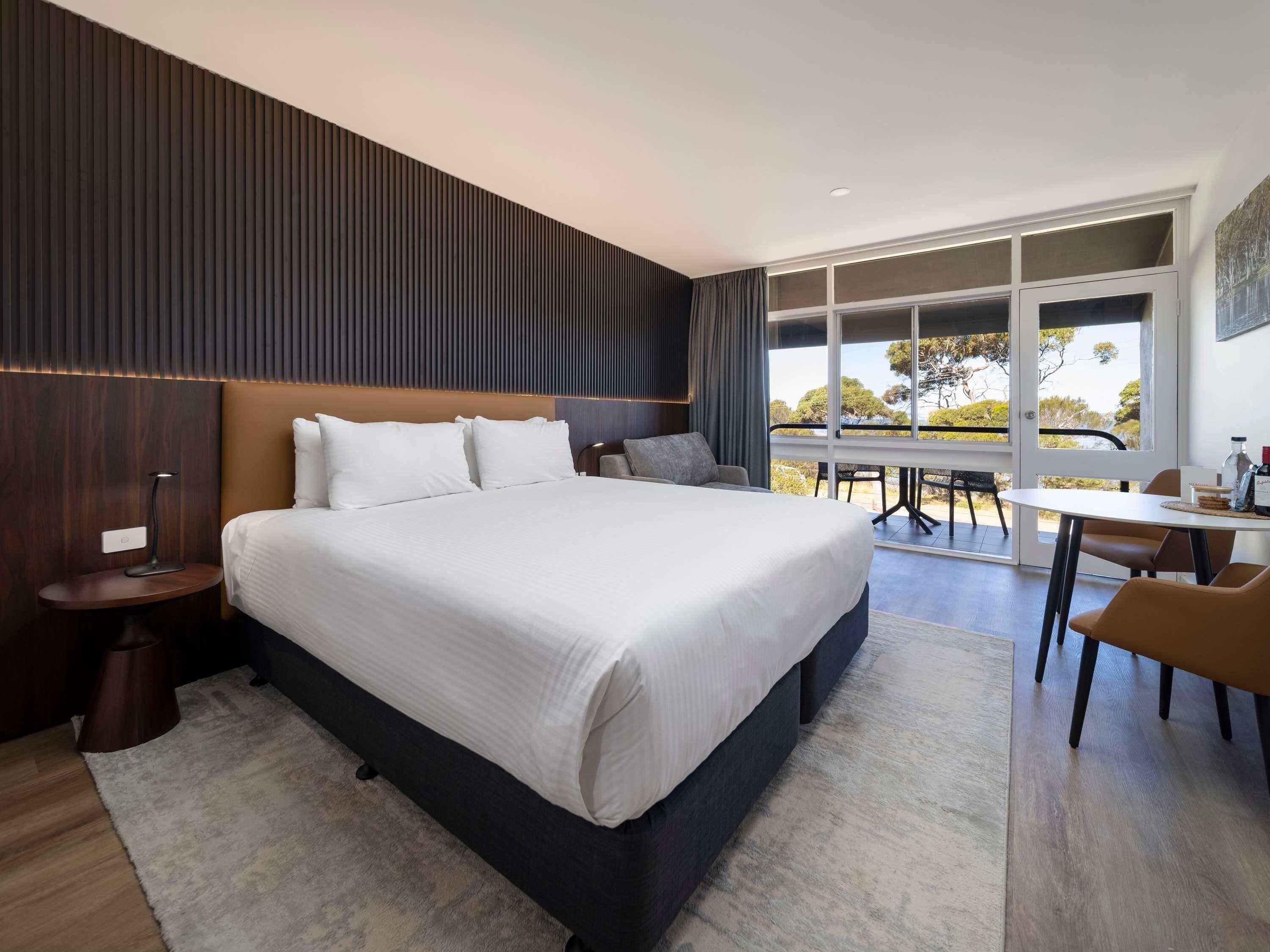 A modern hotel room with a large bed, a desk, and a view of the outdoors.