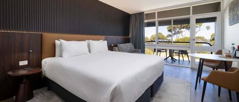 A modern hotel room with a large bed, a desk, and a view of the outdoors.