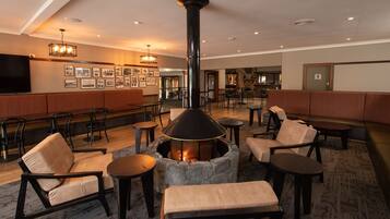 A cozy lounge area with a stone fireplace, comfortable seating, and a bar area in the background.