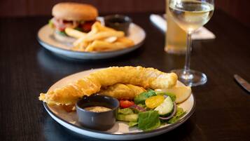 A plate with a salad, chips, and a sandwich, and a glass of white wine on a table.