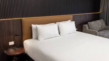 A modern hotel room with a large bed, a bedside table, a lamp, and a grey armchair.