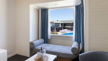 A small room with a window, a sofa, a table with a bottle and glass, and a chair.