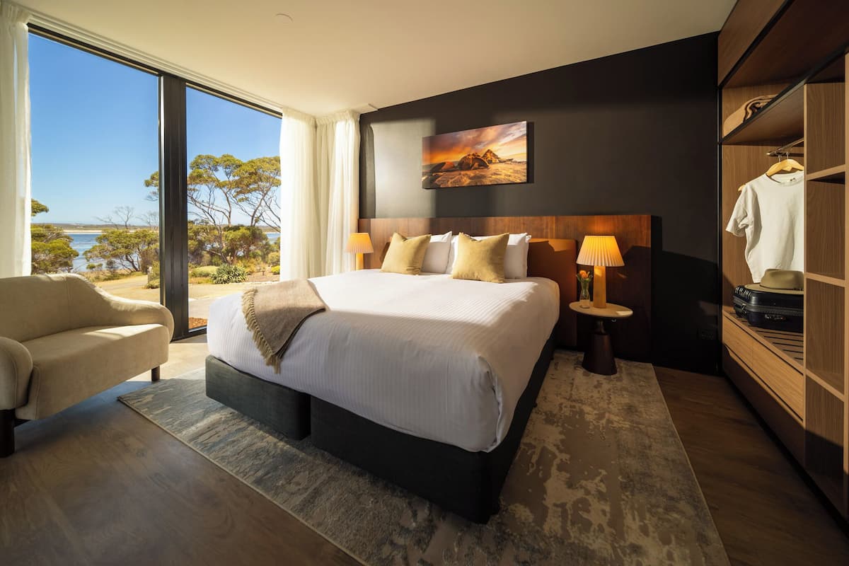 Een moderne hotelkamer met een groot bed, een zithoek, een kledingkast en uitzicht op het omliggende landschap.