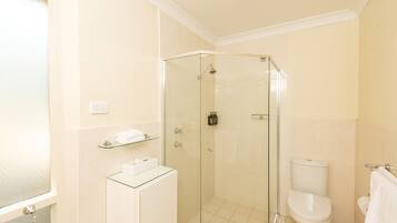 A modern bathroom with a glass-enclosed shower, a white toilet, and a glass-topped sink.
