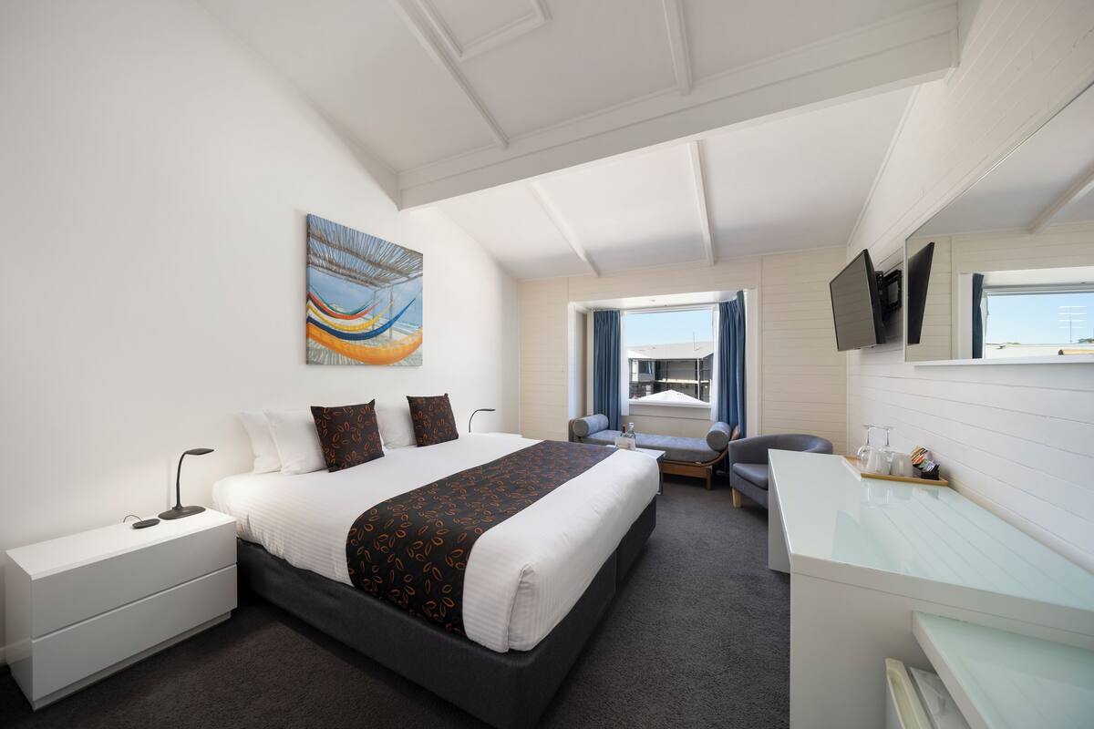 Een moderne hotelkamer met een groot bed, een bureau, een stoel, een televisie en een raam met gordijnen.