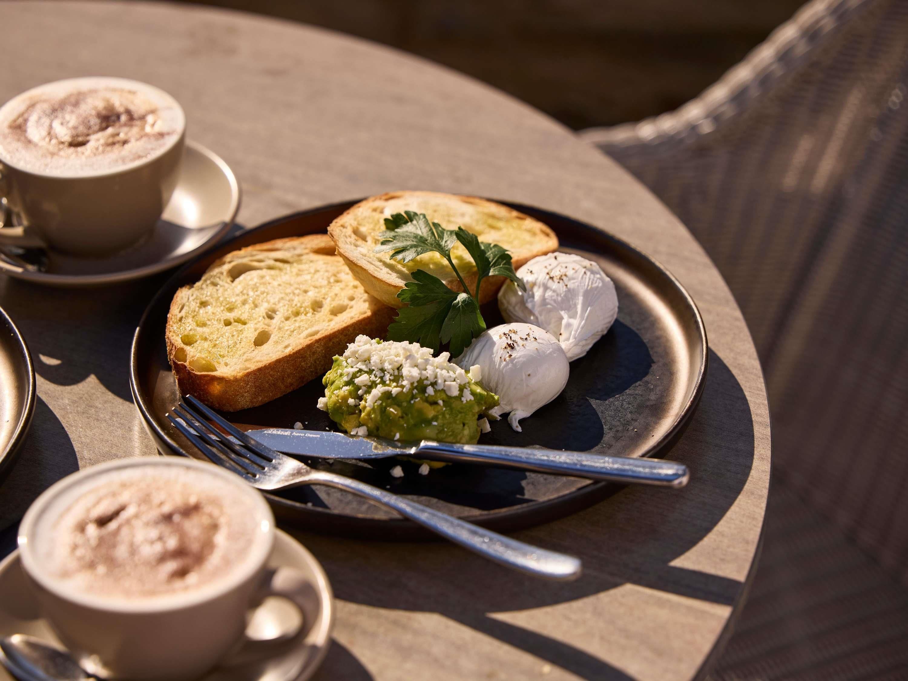 Une assiette avec du pain, du fromage et une pâte à tartiner verte, accompagnée d’une tasse de café.