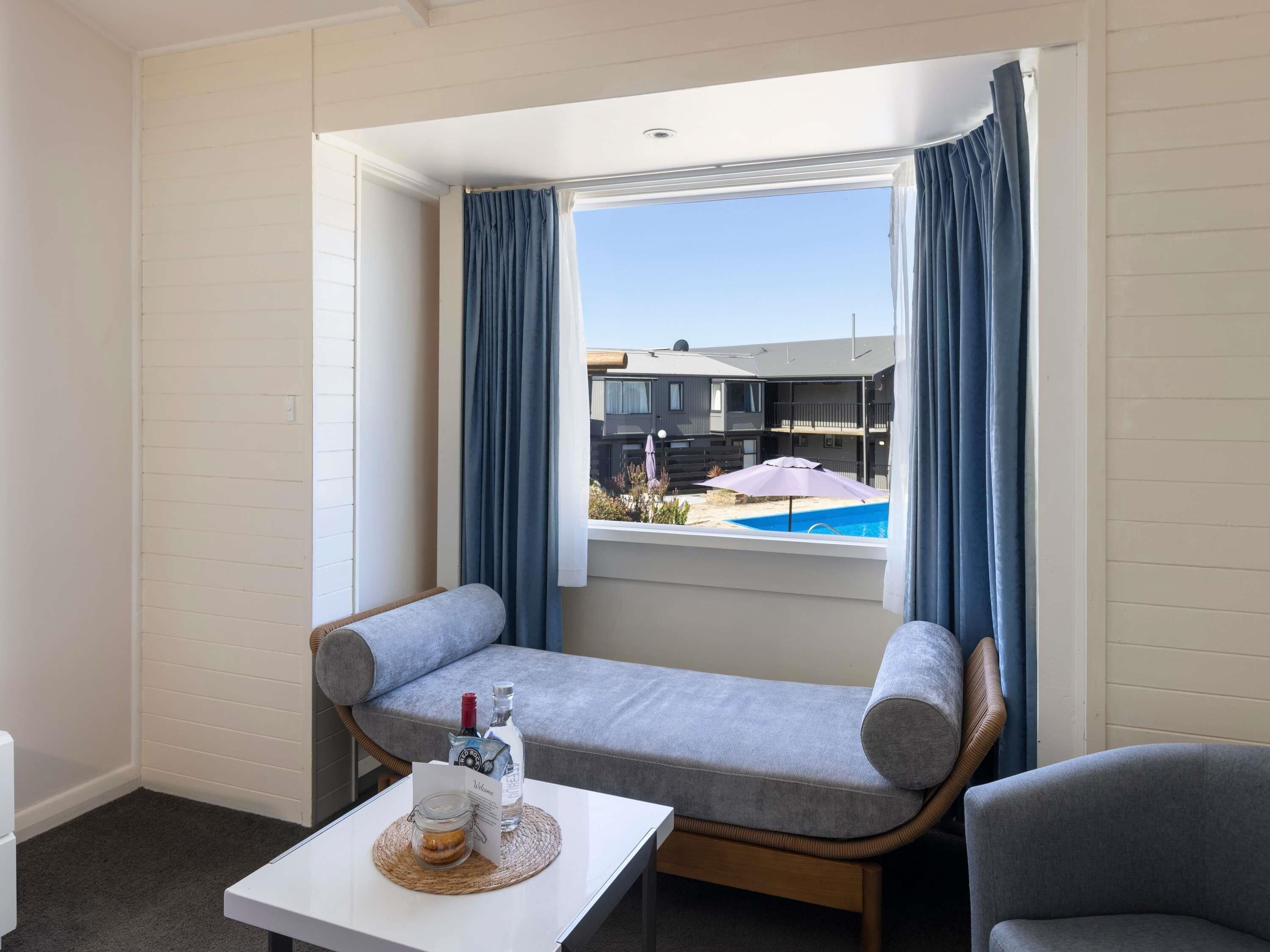 A room with a window, a sofa, a small table, and a bottle of liquor.