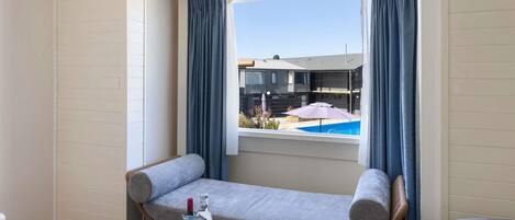 A room with a window, a sofa, a small table, and a bottle of liquor.