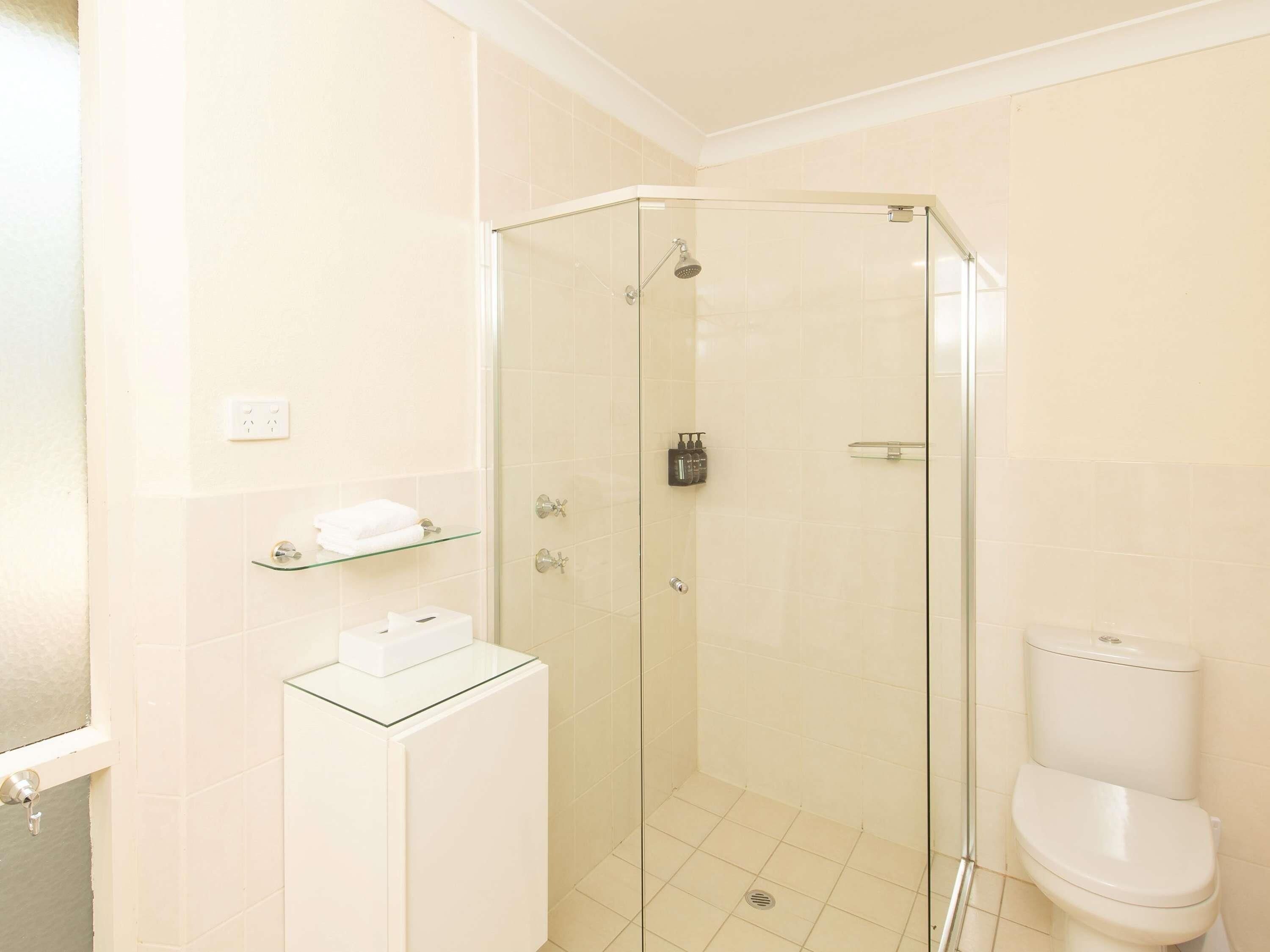 A bathroom with a glass-enclosed shower, a toilet, and a glass-topped vanity with a soap dispenser.