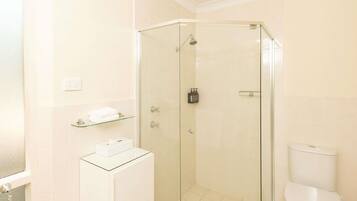 A bathroom with a glass-enclosed shower, a toilet, and a glass-topped vanity with a soap dispenser.
