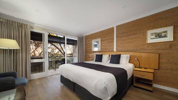 A modern hotel room with a large bed, a desk, a chair, and a view of the outdoors.