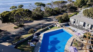 Una propiedad residencial con piscina, camino de entrada pavimentado y vista a una masa de agua extensa.