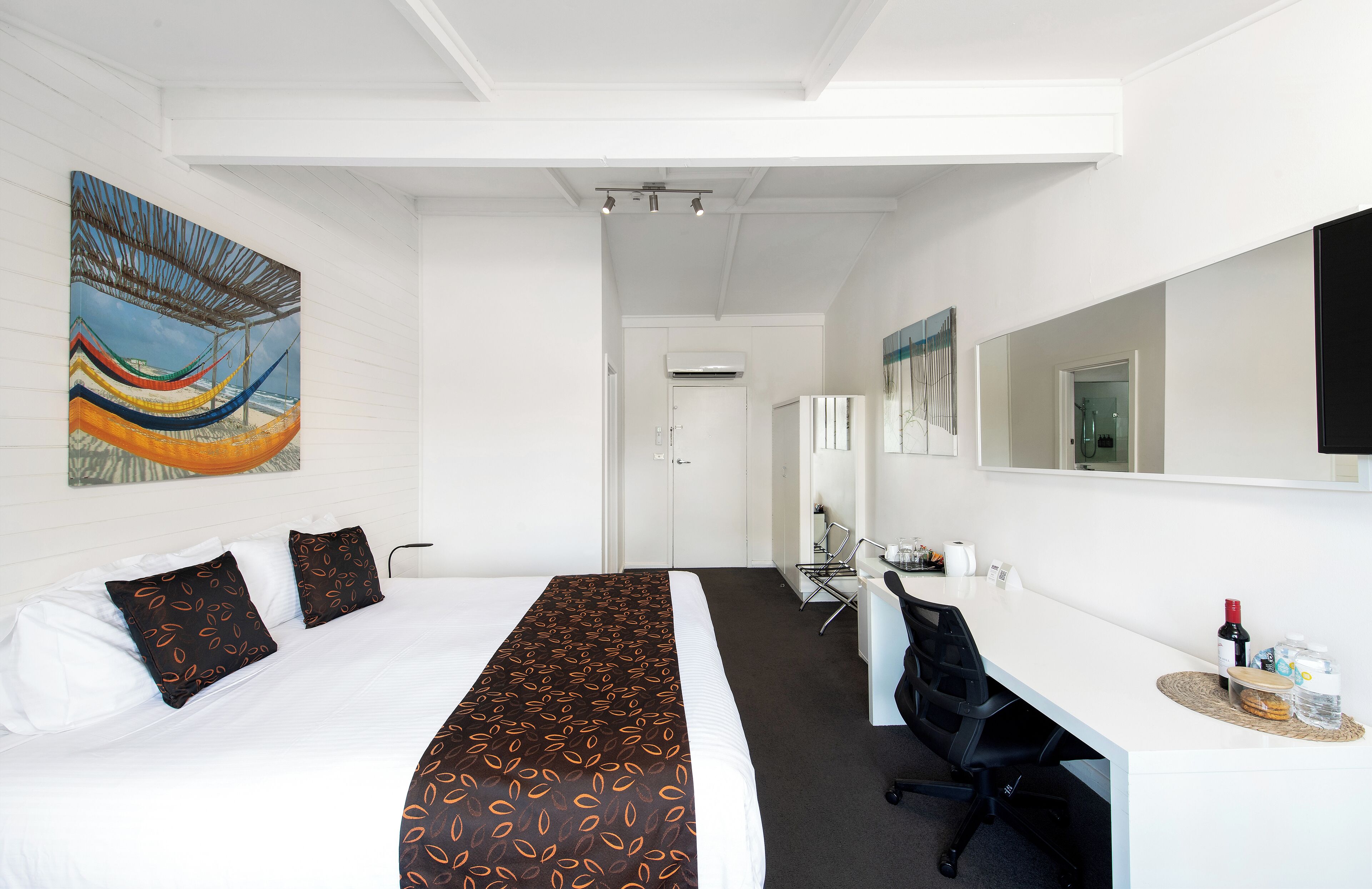 Ein Hotelzimmer mit einem großen Bett, einem Schreibtisch mit Stuhl, einem Spiegel und einem Bild an der Wand.
