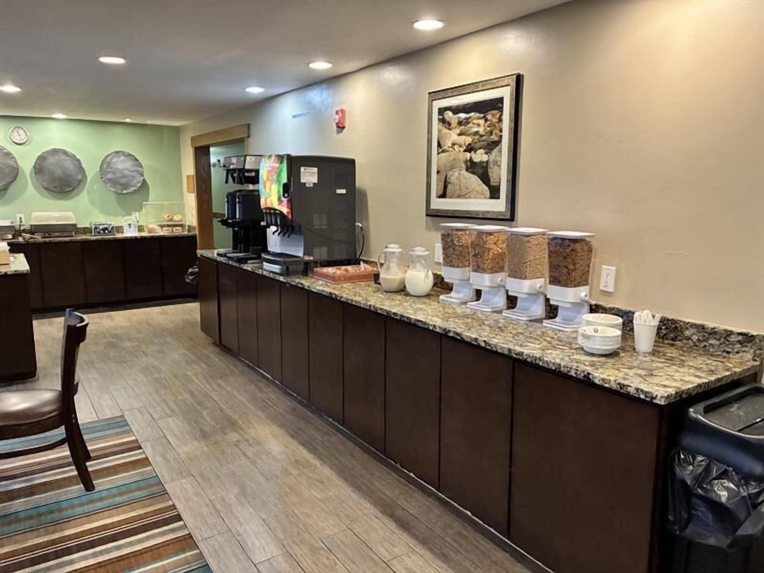Een hotel receptie met een lange balie, koffieautomaten en een koffiehoek met verschillende dranken.
