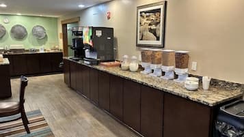 A hotel reception area with a long counter, coffee machines, and a coffee station with various beverages.