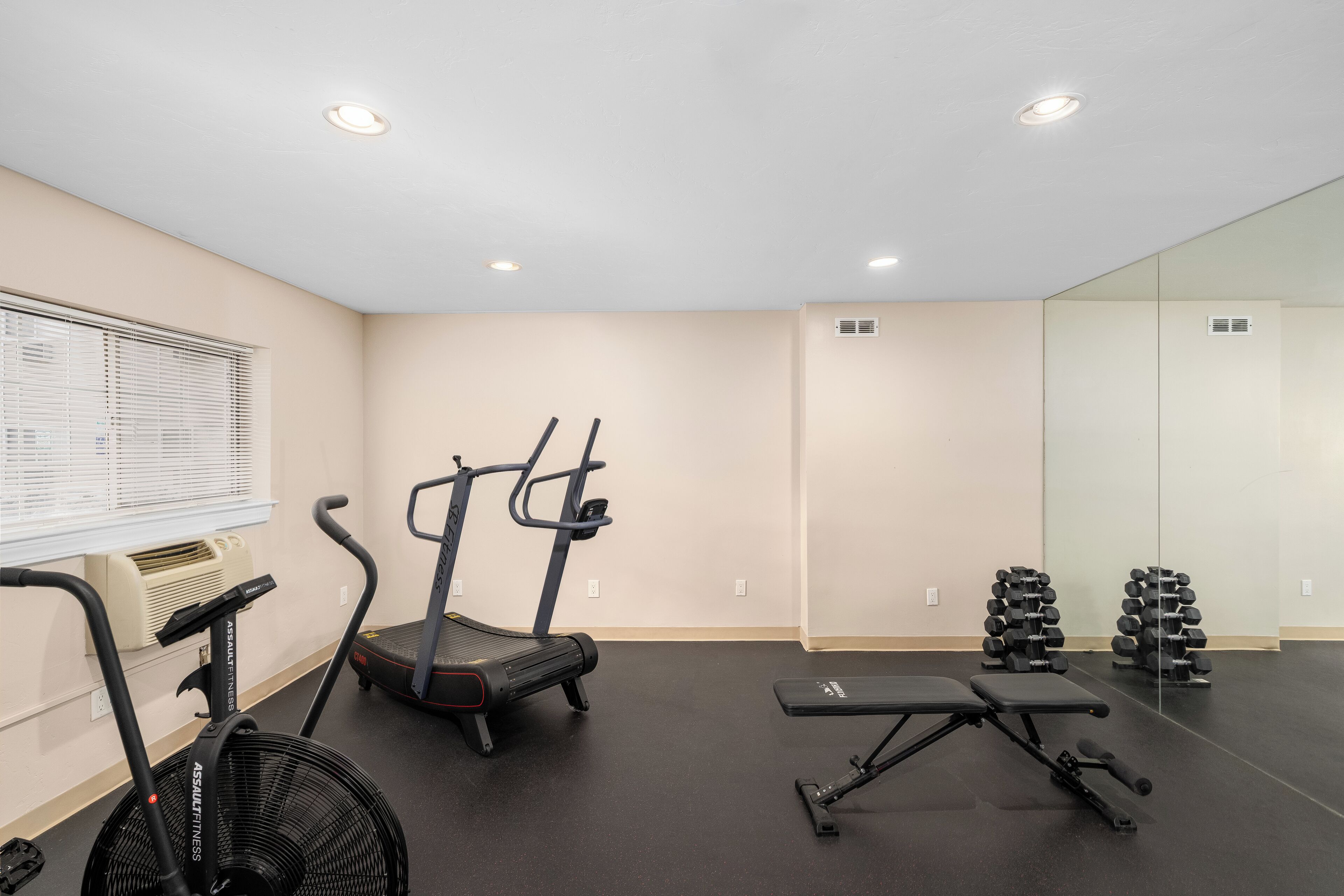 Une salle de sport équipée de tapis de course, d’un appareil elliptique, d’un banc de musculation et d’un ventilateur.