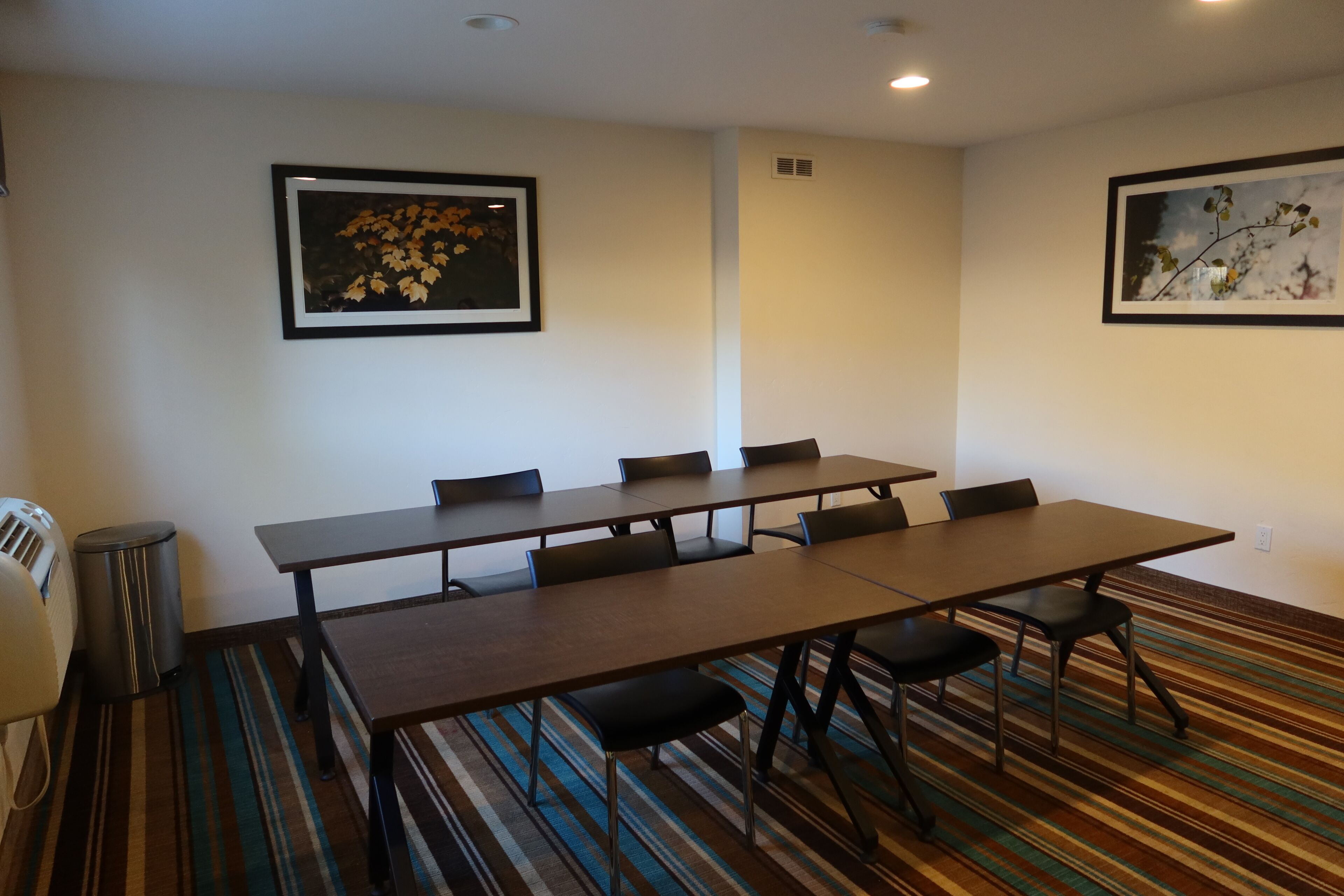 A conference room with a long table, six chairs, and two framed pictures on the walls.
